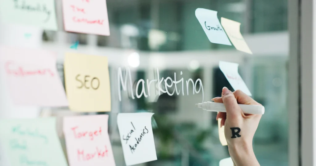 Marketing, hand writing on glass wall with sticky notes for business growth, seo plan or target audience trends, and strategy goals for brand campaign.
